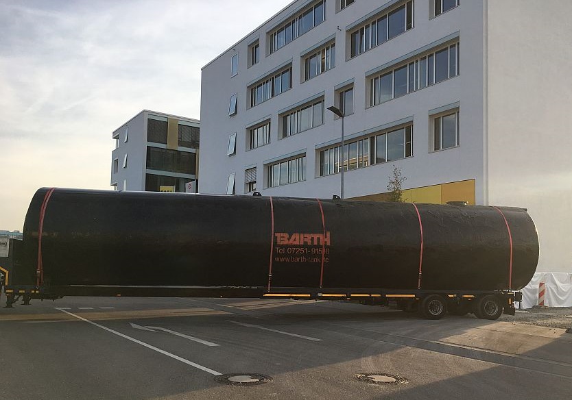 ein schwarzer 100.000 Liter Erdtank f&uuml;r Regenwasser von der Firma Tank und Apparate Barth GmbH wird auf einem LKW auf die Baustelle angeliefert